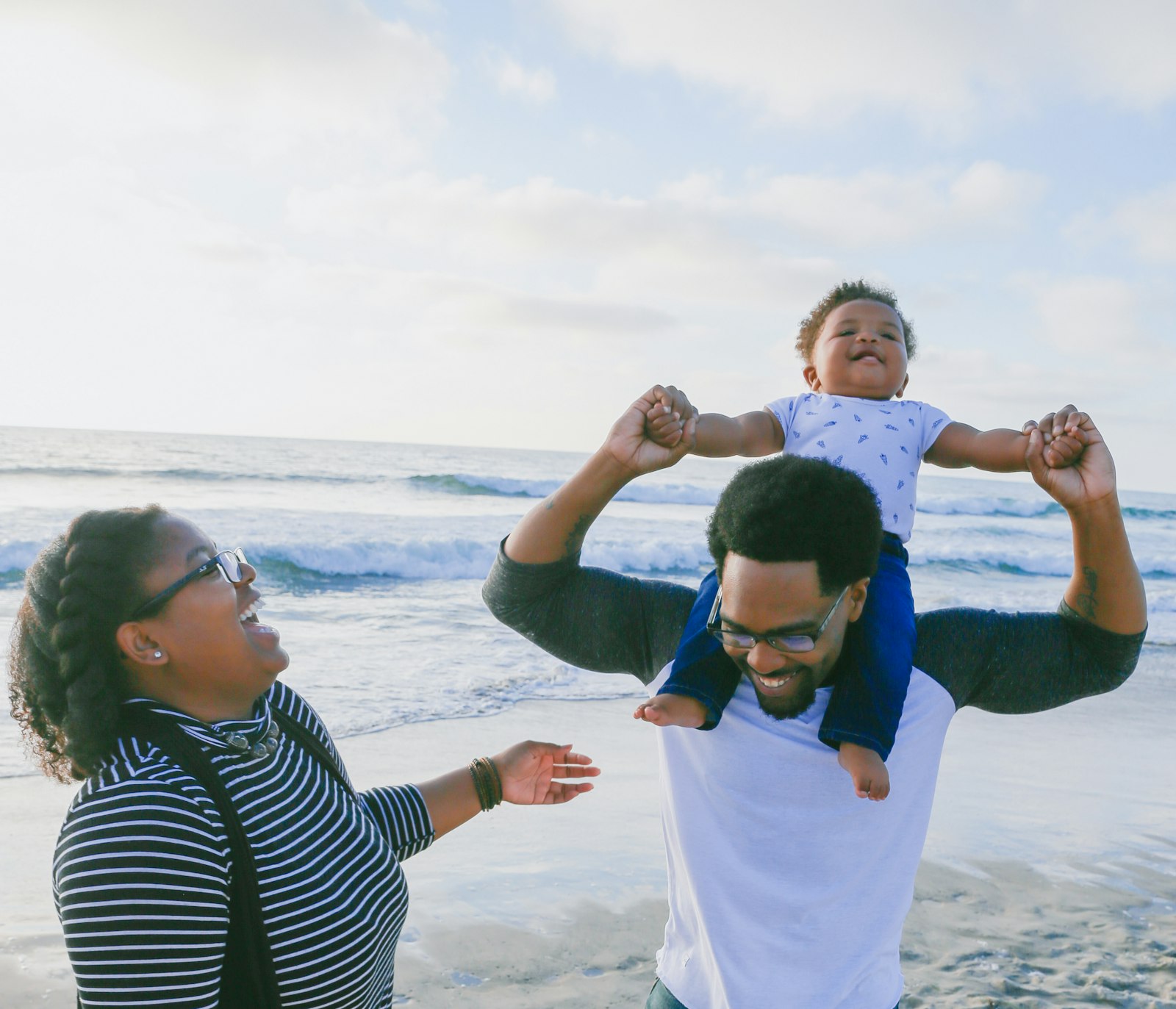 Father lifting his baby on his shoulders on a beach as the mother laughs